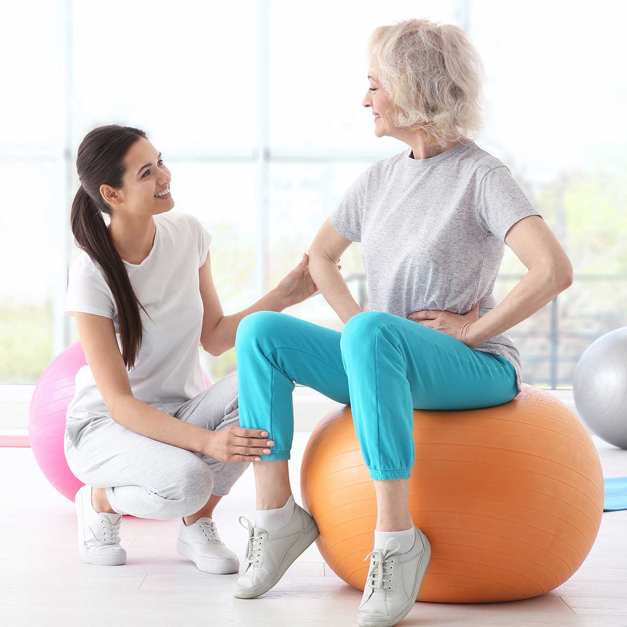 photo of woman balancing on exercise ball with the help of a physical therapist